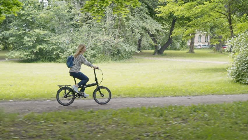 The girl is riding a folding bicycle in the park