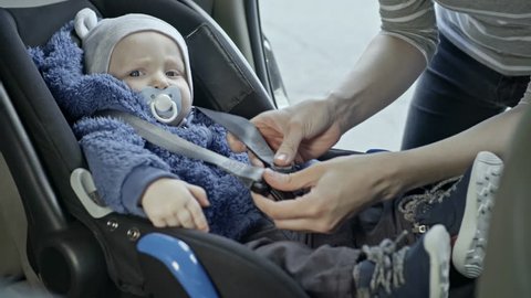 Tilt down of mother putting little baby into car seat and fastening belt