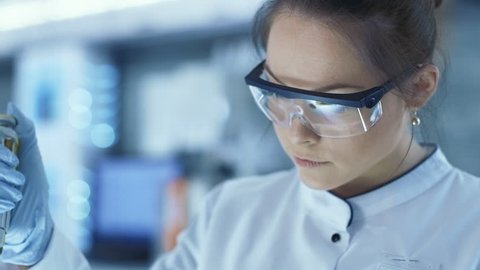 Female Research Scientist Uses Micropipette Filling Test Tubes in a Big Modern Laboratory. In the Background Scientists are Working. Shot on RED EPIC-W 8K Helium Cinema Camera.