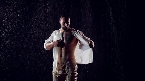 muscular male bodybuilder takes wet body white shirt standing in the night under a big rain. large inflated Breasts