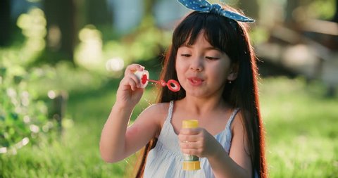 Happy little Asian girl blowing soap bubbles in spring Park. Slow motion