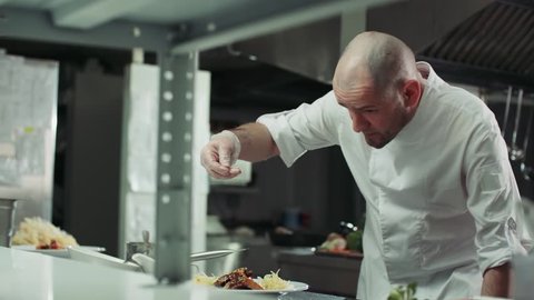 Asian chef serves a dish of meat on a plate adding the final spices slow motion