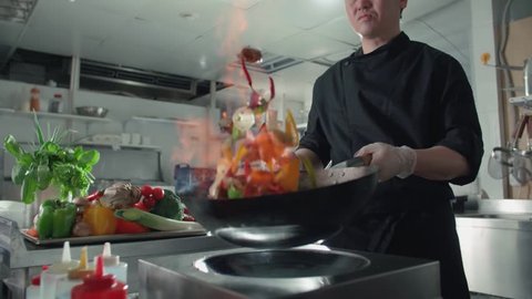 chef works mixed colored roasting vegetables in the wok-tossing and flames , kitchen Asian restaurant, slow motion