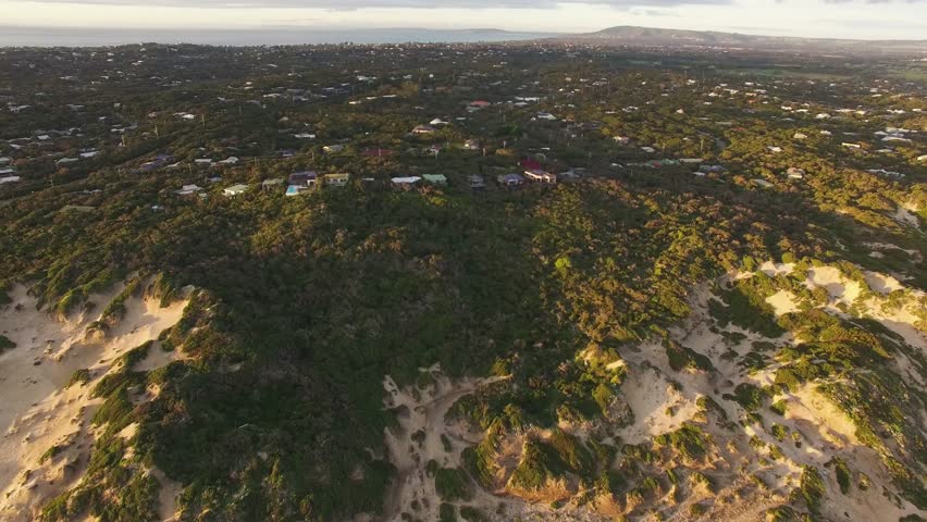 Forward flight towards vacation homes in lush coastal vegetation on Mornington Peninsula coastline at sunset. Melbourne, Australia