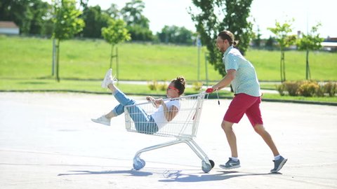 Husband and wife came for shopping. While the children are not at home, they are having fun. Adults are like children. Sense of humor. Fun in the parking. Shopping cart for a supermarket