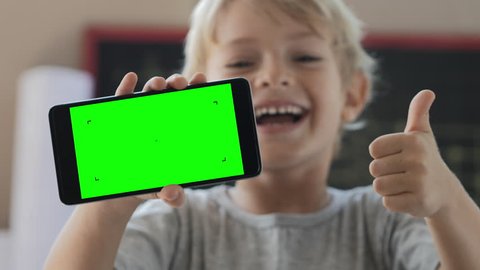 Cute child showing phone with green screen, laughing and showing thumbs up. Idea of very funny video or picture on display. 