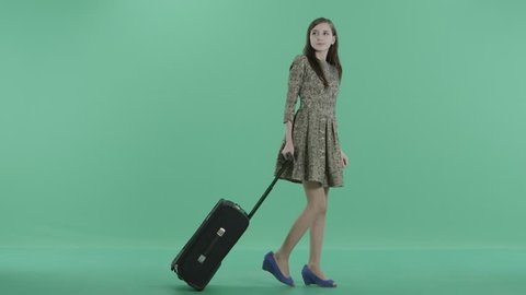a pretty girl in dress is walking with luggage and smiling