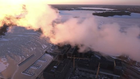 The aerial shot of the urban city of Helsinki with the white smoke coming from the top of the pipe in the factory