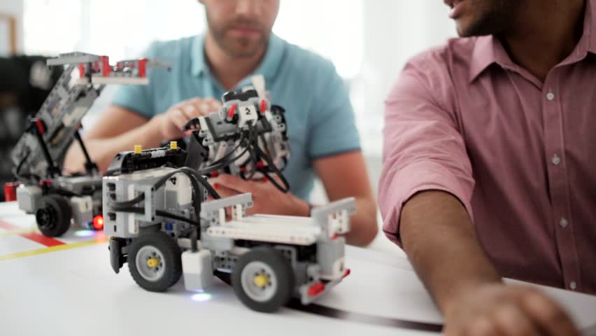 Two young professionals constructing robot and looking at laptop