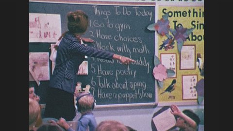 1970s: Teacher stands in classroom at blackboard, points to blackboard. Children raise hands. Children look around, teacher sits next to child, reads books to children. Children play with puppets.