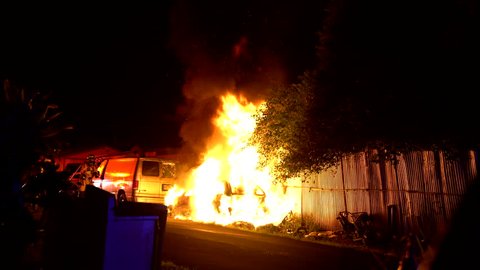 Fire fighters arrive to a vehicle on fire and fully engulfed in flames at night.  Fire fighters extinguish the burning vehicle with high pressure hoses.