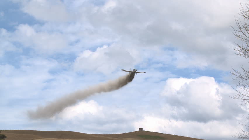 Crop dusting over a farm a  plane drops its load of fertilizer