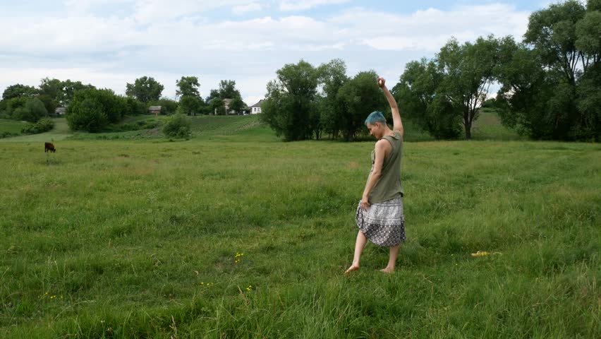 The girl is doing a handstand in the field. A merry girl is tumbling on the grass.