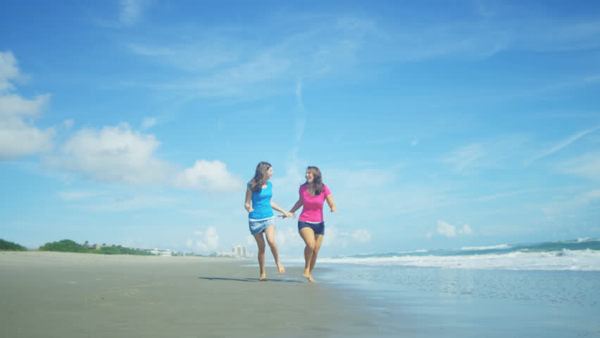 Attractive Caucasian American sisters running on the beach in colourful clothes for fun together on holiday RED EPIC