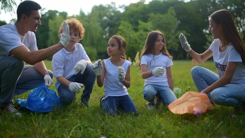 Cheerful kids helping volunteers with picking up plastic bottles outdoors