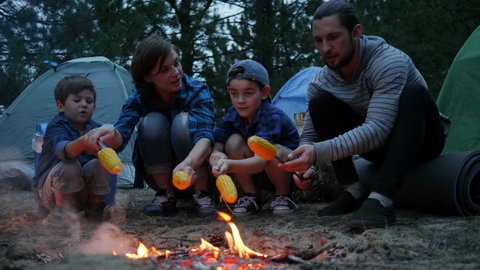 Picnic at night evening outdoors, American family around fire prepare yellow maize in forest 庫存影片