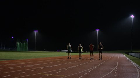 Competitive male athletes running at race track in the dark. Slow motion.