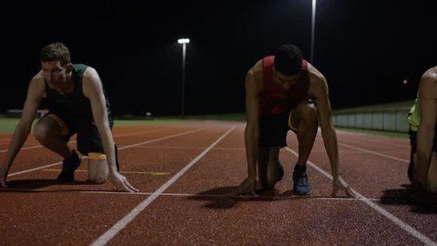 Competitive male athletes running at race track in the dark. Slow motion.