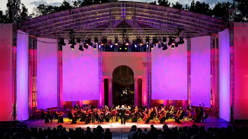 Symphony orchestra performing outdoors at open public event at night. Night scene, illuminated stage. Royalty-Free Stock Footage #29193931