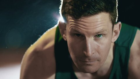 Close up on face of male runner at athletics track crouching at the starting blocks before a race. In slow motion.