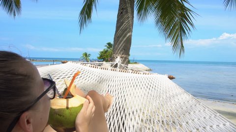 Young Woman Swinging in Hammock with Coconut. Vacation in Paradise