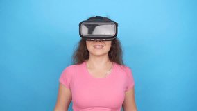 Happy young woman using a virtual reality headset on blue background