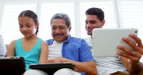Happy family sitting on sofa and using laptop, mobile phone and digital tablet in living room