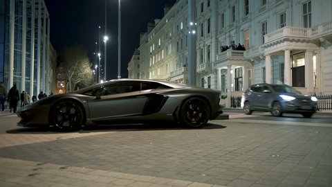 LONDON, UNITED KINGDOM - CIRCA 2017: Rich businessmen party on the balcony with unique luxury super-car parked on Exhibition Rd, Kensington London. Lamborghini Aventador is a mid-engine sports car
