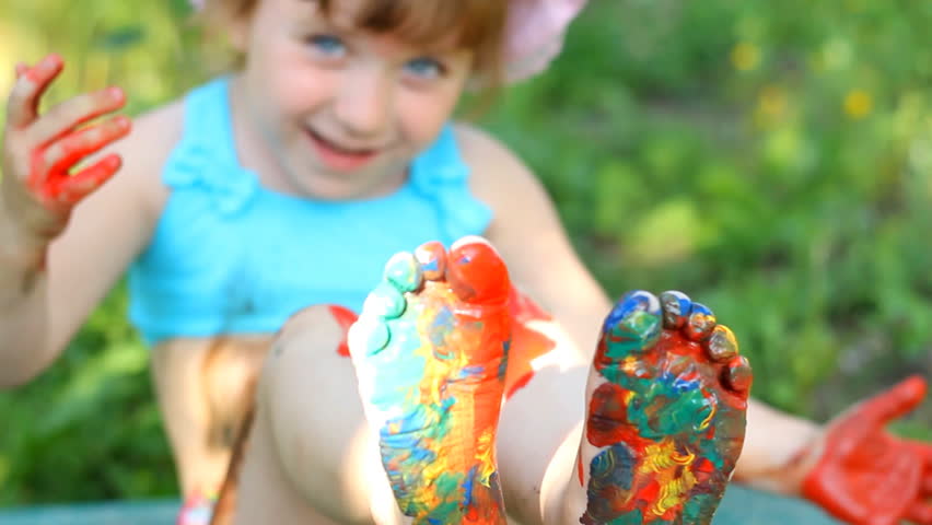 The child is sitting on the nature paint with paints and shows his legs.