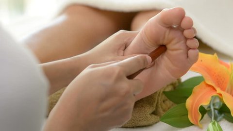 Professional therapist giving relaxing reflexology Thai foot massage with stick to a woman in spa