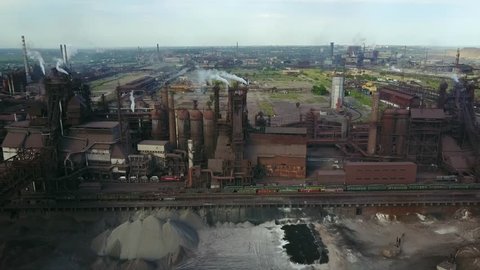 Aerial view over industrialized city with air atmosphere and river water pollution from metallurgical plant near sea. Dirty smoke and smog from pipes of steel factory and blast furnaces. Ecological