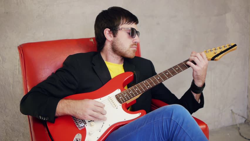Close-up of musician sitting on armchair and playing on guitar