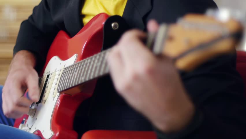 Male hands playing song on red electric guitar