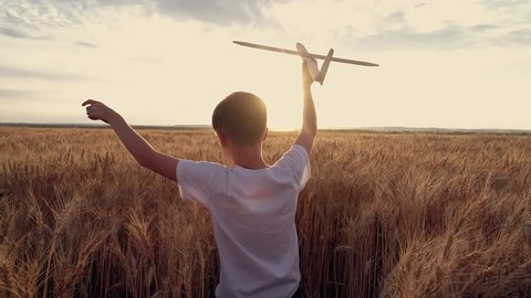 Happy kid run with a toy airplane at sunset over a wheat field. The kid dreams of becoming an astronaut pilot. Airplane pilot. Children's dream to run with a toy. Kid airplane pilot. Dream concept