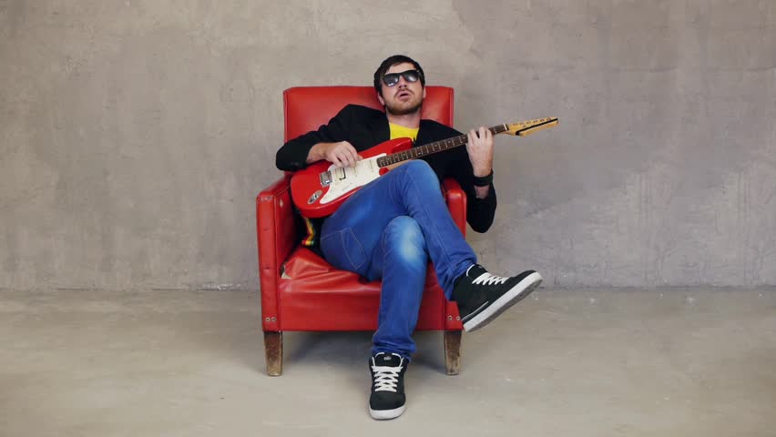 Guitarist sitting on armchair and playing solo on guitar