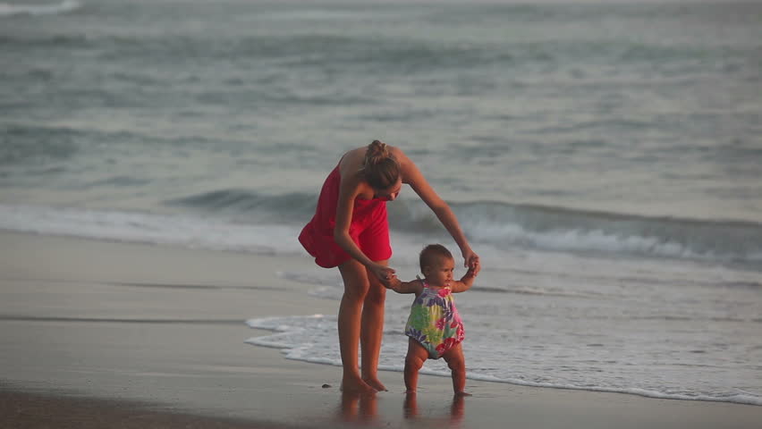 Pretty woman in red dress walking with baby on coast