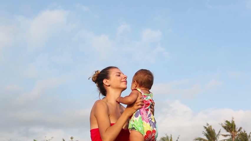 Beautiful playful woman raising with her baby while summer holiday
