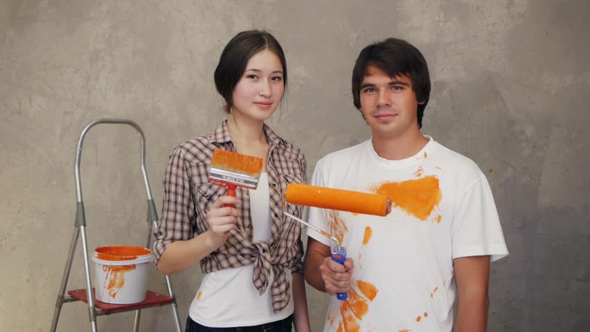 Attractive couple holding brushes and discussing remodeling flat