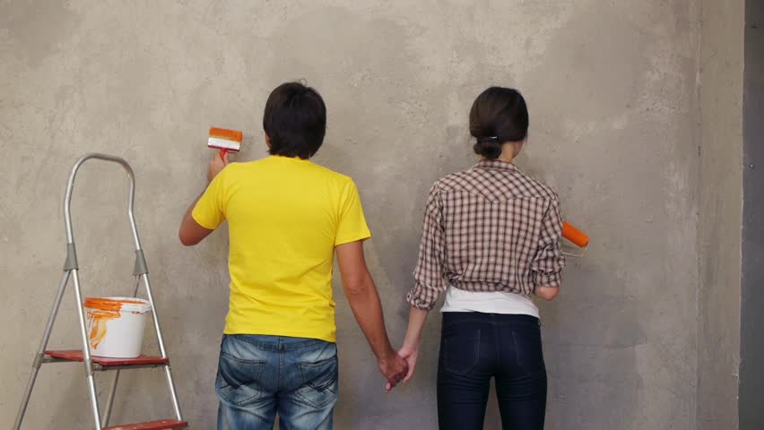 Lovely couple holding by hands and painting wall