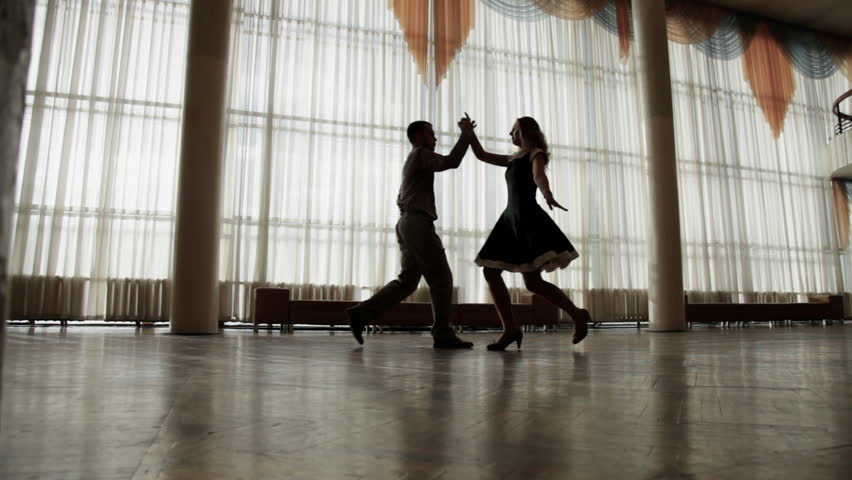 Attractive couple training to dance together. Silhouettes. Dolly shot. 