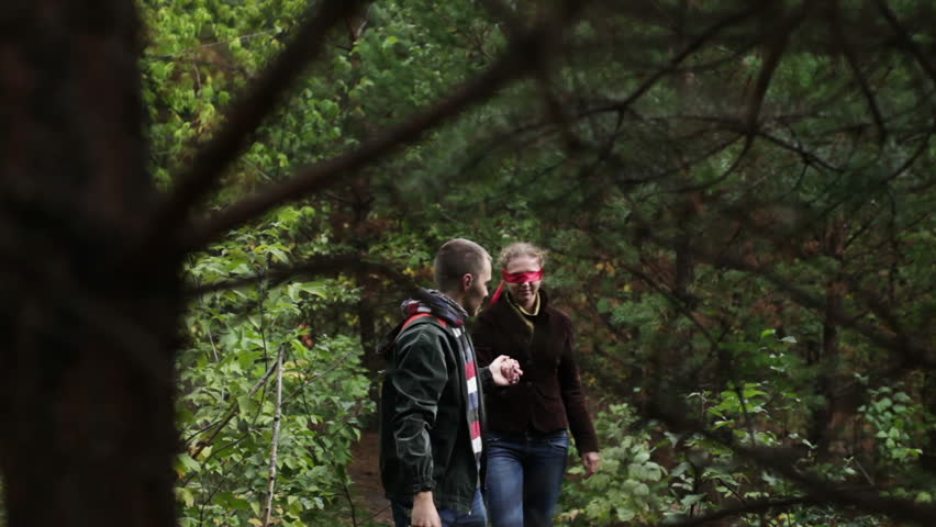 Man leads blindfolded woman in forest