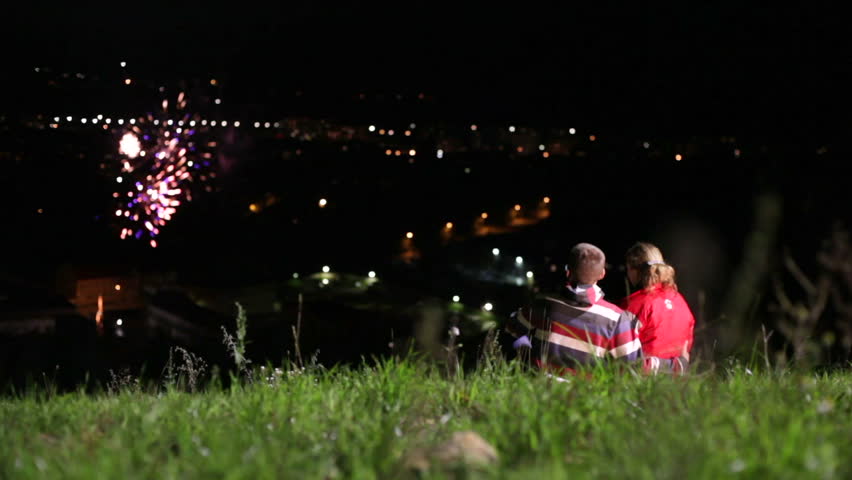 Couple sitting on meadow and looking at firework