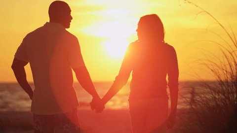 Silhouette of loving ethnic couple holding hands and enjoying sunset on beach vacation  – Stockvideo