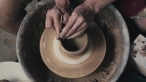 Potter shapes the clay product with pottery tools on the potter's wheel, top view, toned cinematic, craft factory authentic