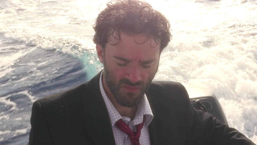 Man in suit with a briefcase eating a peach and throwing the pit in the water while driving a boat in the middle of the sea