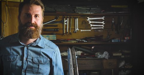 Portrait of a successful well-groomed handsome bearded master hipster, specialist in bicycles, repairing a bicycle in his workshop, wheels, frame, wrench. Concept: pro bike, cycle passion, lifestyle.