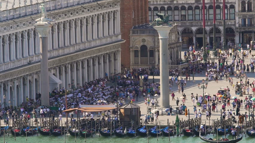 Colonnade building facing busy square with two columns, gondolas by riverbank