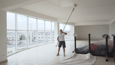Ethnic worker painting walls in a hall with roller, camera on glidecam moving around