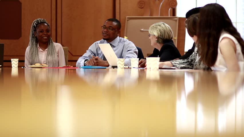 Relaxed and happy business meeting with creative, diverse team of entrepreneurs. In modern board room with reflections on table. Multi-ethnic and natural in 4K.