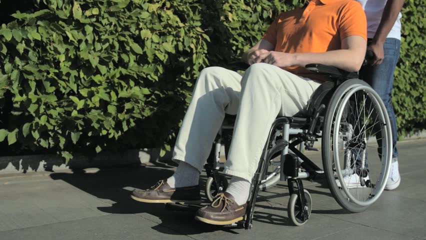 Tracking shot of a nice man walking with a wheelchaired man